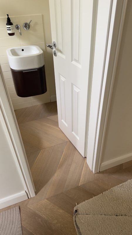 Chevronparkett läuft ohne sichtbare Übergangsschiene vom Flur durch die Tür ins Gäste-WC