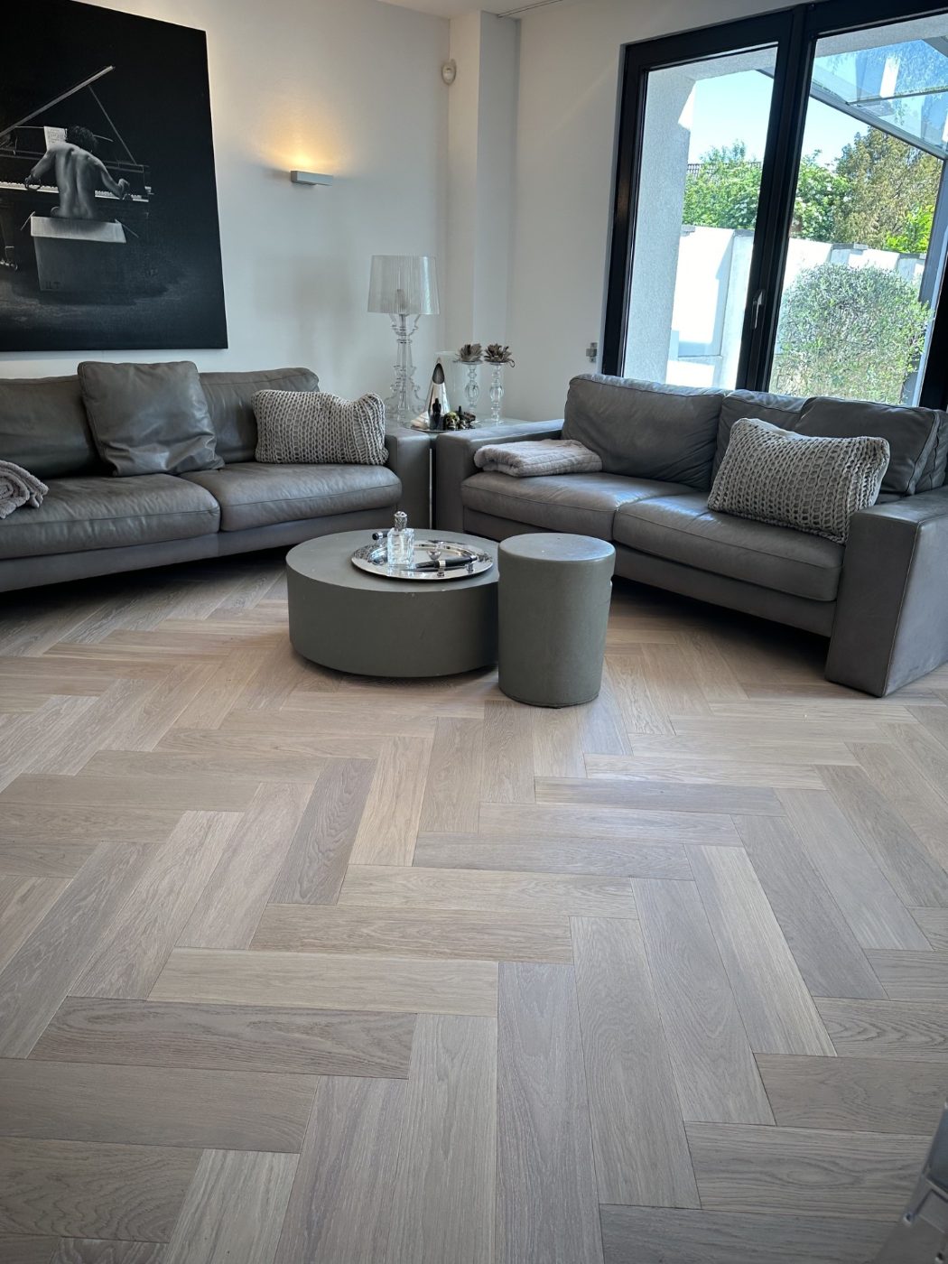 Wohnzimmer mit weißem Fischgrätparkett aus Eiche und grauen Sofas